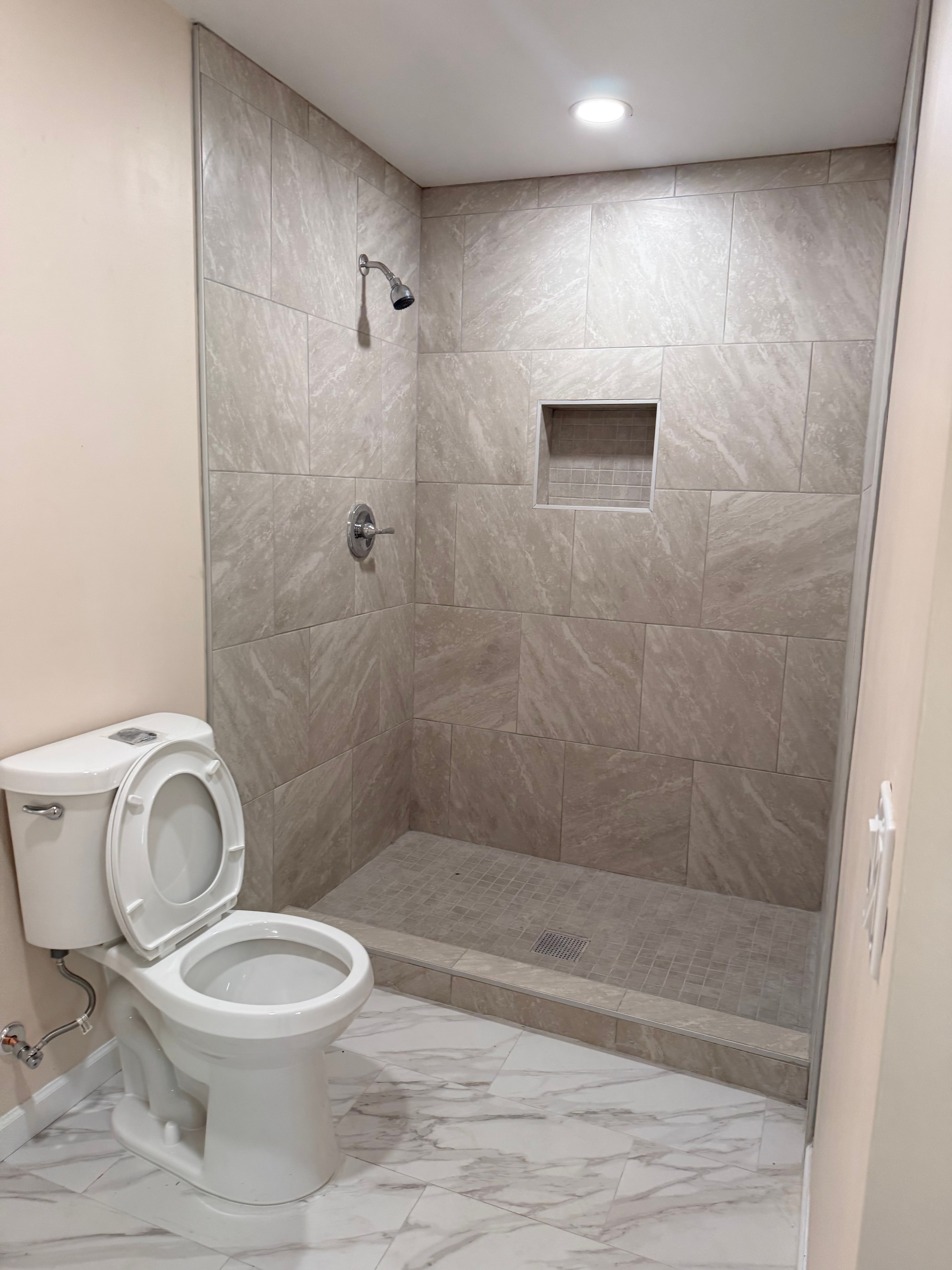 Restored bathroom with large format tile shower and marble accent wall