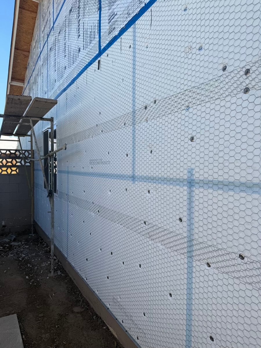 White mesh house wrap with blue straps — RMSERVCORP weatherproofing